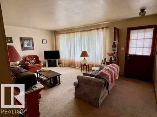 Living area featuring neutral wall paint, light-colored carpeting, and a full-length window with sheer curtains - 5454 46 Street, Vegreville, AB - Indoor Photo Showing Living Room