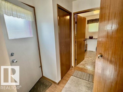 Entryway featuring wood-finish flooring, a solid white exterior door with a textured glass insert, and a closet with a wood-panel door - 5454 46 Street, Vegreville, AB - Indoor Photo Showing Other Room