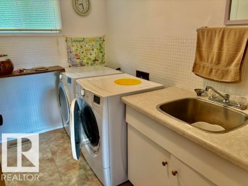 Dedicated laundry area featuring a utility sink with a laminate countertop, white cabinetry with bronze-finish hardware, and tiled walls - 5454 46 Street, Vegreville, AB - Indoor Photo Showing Laundry Room
