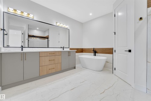 Spacious bathroom featuring a freestanding tub with matte black fixtures, a dual-sink vanity with light gray and wood-finish cabinetry, a large frameless mirror, and large format marble-look floor tiling - 2027 156 Avenue, Edmonton, AB - Indoor Photo Showing Bathroom