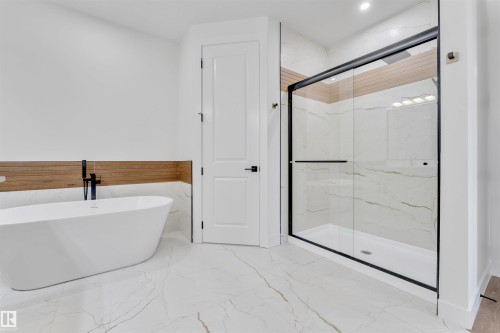 Modern bathroom featuring a freestanding soaking tub with a matte black faucet, a spacious glass-enclosed shower with a black frame, and wood-finish wall paneling - 2027 156 Avenue, Edmonton, AB - Indoor Photo Showing Bathroom