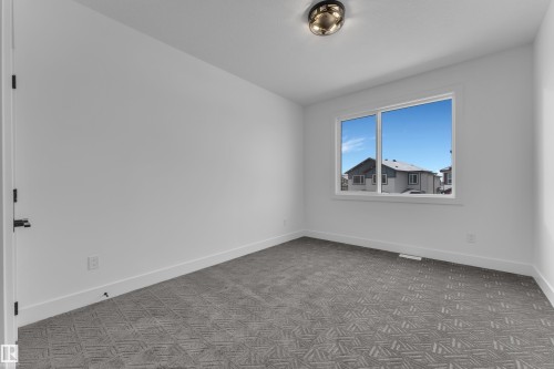 Bright room featuring a large window, patterned carpet flooring, white baseboards, and a contemporary flush-mount ceiling light fixture - 2027 156 Avenue, Edmonton, AB - Indoor Photo Showing Other Room