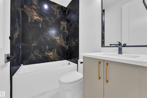 Bathroom featuring a tub/shower combination with black marble-effect wall tiling, a vanity with a white countertop and undermount sink, and a framed mirror - 2027 156 Avenue, Edmonton, AB - Indoor Photo Showing Bathroom