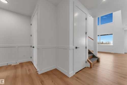 Entryway featuring crisp white wainscoting, wood-finish flooring, and a staircase with wood railing and carpeted treads - 2027 156 Avenue, Edmonton, AB - Indoor Photo Showing Other Room