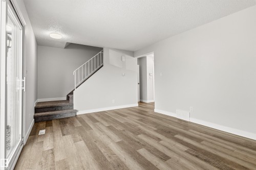 Open living space featuring wood-finish flooring, a contemporary staircase with white railing, and a sliding glass door - 707 Clareview Road, Edmonton, AB - Indoor Photo Showing Other Room