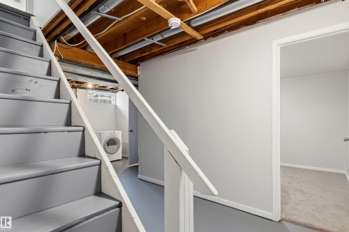Painted stairs with a white handrail lead to a finished lower level featuring light gray walls, a window with glass block, and a carpeted room beyond an open doorway - 707 Clareview Road, Edmonton, AB - Indoor Photo Showing Laundry Room
