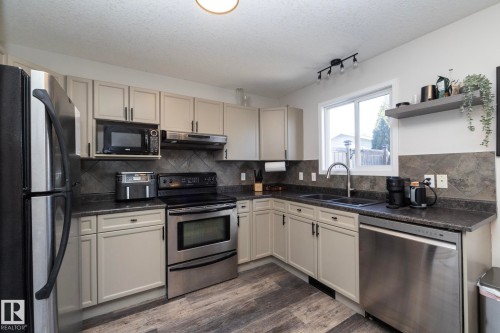 Modern kitchen featuring light-toned cabinetry with dark hardware, dark countertops, and a full tile backsplash - 4204 161 Avenue, Edmonton, AB - Indoor Photo Showing Kitchen With Stainless Steel Kitchen With Double Sink