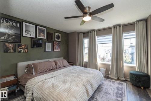 Spacious bedroom featuring wood-finish flooring, a contemporary ceiling fan with integrated lighting, and a wall of three large windows - 4204 161 Avenue, Edmonton, AB - Indoor Photo Showing Bedroom