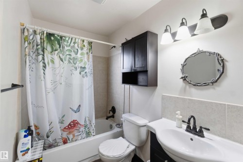 Bathroom featuring a white bathtub, tiled shower surround, and a wall-mounted vanity with a white sink - 16 Michigan Street, Devon, AB - Indoor Photo Showing Bathroom