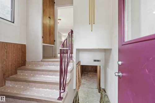 Staircase featuring patterned risers, wood-finish paneling, and a metal railing - 16 Michigan Street, Devon, AB - Indoor Photo Showing Other Room