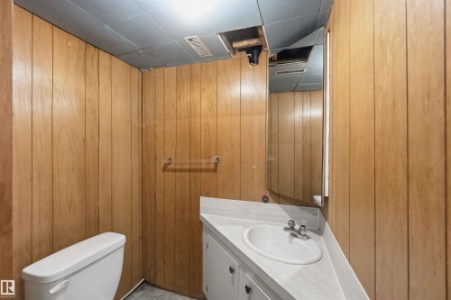 Bathroom featuring wood paneling, a white toilet, and a vanity with an integrated sink and mirror - 16 Michigan Street, Devon, AB - Indoor Photo Showing Bathroom