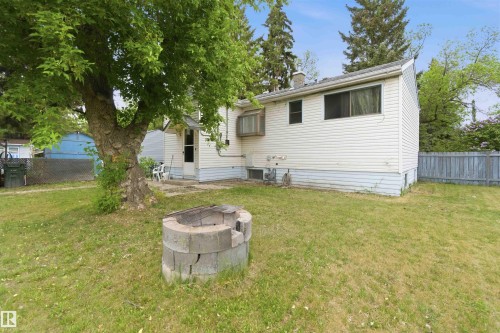 Spacious backyard featuring a substantial mature tree, a block-constructed fire pit, a white vinyl-sided exterior, and a rear entrance - 16 Michigan Street, Devon, AB - Outdoor