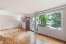 Spacious room featuring wood-finish flooring, a large picture window, and a paneled entry door with an arched transom window - 16 Michigan Street, Devon, AB  - Indoor Photo Showing Other Room 