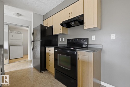 Kitchen featuring light wood-finish cabinetry, black appliances, dark countertops, and tiled flooring - 312 13908 136 Street Nw, Edmonton, AB - Indoor Photo Showing Kitchen