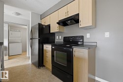 Kitchen featuring light wood-finish cabinetry, black appliances, dark countertops, and tiled flooring - 