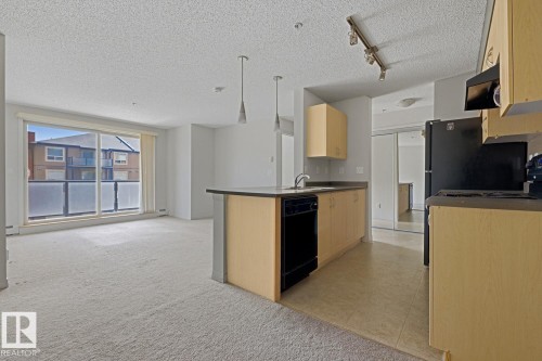 Open-concept living area featuring a kitchen island, track lighting, and a full-height sliding glass door - 312 13908 136 Street Nw, Edmonton, AB - Indoor Photo Showing Kitchen