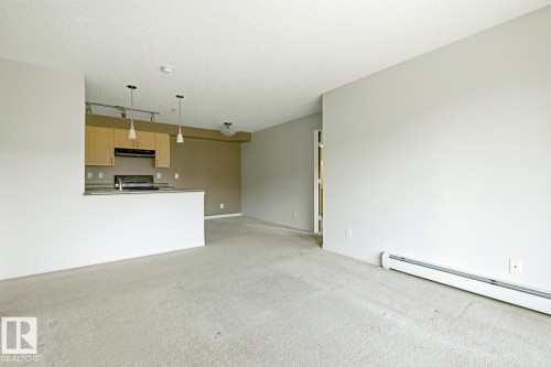 Open-concept living space featuring light-toned carpeting, a kitchen with light wood cabinetry, track lighting, and pendant fixtures - 312 13908 136 Street Nw, Edmonton, AB - Indoor Photo Showing Kitchen