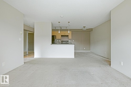 Open concept living area featuring light-toned carpet flooring and a kitchen with light wood cabinetry, a breakfast bar, and pendant lighting - 312 13908 136 Street Nw, Edmonton, AB - Indoor Photo Showing Kitchen