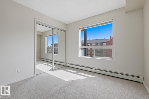 Bright room featuring light grey carpeting, a large window, and mirrored sliding closet doors - 312 13908 136 Street Nw, Edmonton, AB - Indoor Photo Showing Other Room