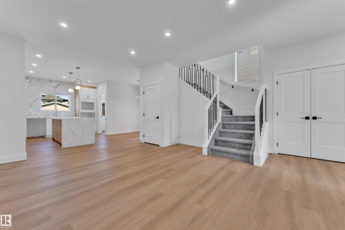 Open-concept living space featuring wood-finish flooring, recessed lighting, and a staircase with carpeted treads and black metal railings - 6092 179 Ave Nw, Edmonton, AB - Indoor Photo Showing Other Room