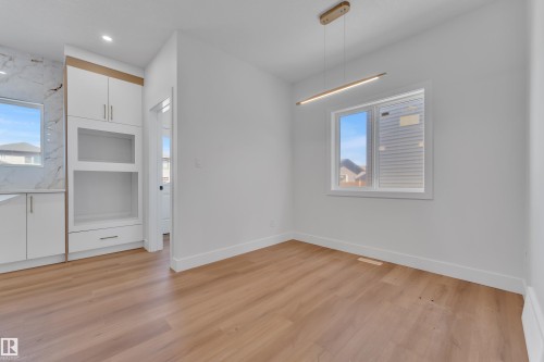 Bright interior space featuring wood-finish flooring, a contemporary linear chandelier, and a large window - 6092 179 Ave Nw, Edmonton, AB - Indoor Photo Showing Other Room