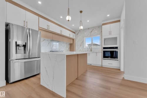 Modern kitchen featuring a waterfall island with a light-toned countertop, light wood-finish flooring, and white cabinetry with wood accents - 6092 179 Ave Nw, Edmonton, AB - Indoor Photo Showing Kitchen