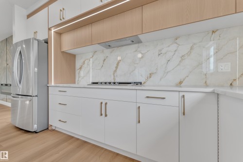 Contemporary kitchen featuring white cabinetry with gold-tone hardware, a large format marble-look backsplash, and a stainless steel refrigerator - 6092 179 Ave Nw, Edmonton, AB - Indoor Photo Showing Kitchen