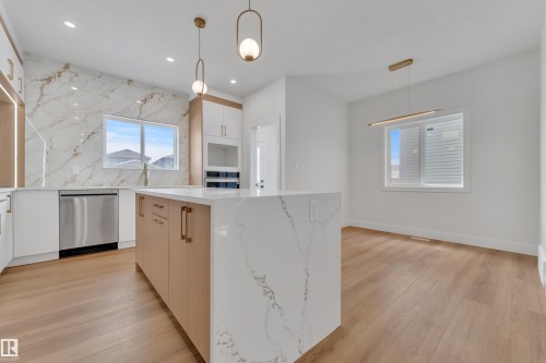 Modern kitchen featuring a waterfall-edge island, full-height decorative slab backsplash, stainless steel dishwasher, wood-finish flooring, and contemporary pendant lighting - 6092 179 Ave Nw, Edmonton, AB - Indoor Photo Showing Kitchen