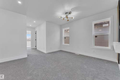 Spacious interior room featuring light gray patterned carpeting, white walls, two windows with white trim, a contemporary sputnik-style ceiling fixture, and recessed lighting - 6092 179 Ave Nw, Edmonton, AB - Indoor Photo Showing Other Room