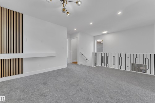 Open-concept upstairs area featuring light gray carpeting, a contemporary black and gold chandelier, recessed lighting, a modern wood slat accent wall with a built-in shelf, and a sleek metal railing - 6092 179 Ave Nw, Edmonton, AB - Indoor Photo Showing Other Room