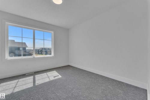 Room featuring a large grid-pattern window, white trim throughout, textured gray carpeting, and a flush-mount ceiling light fixture - 6092 179 Ave Nw, Edmonton, AB - Indoor Photo Showing Other Room