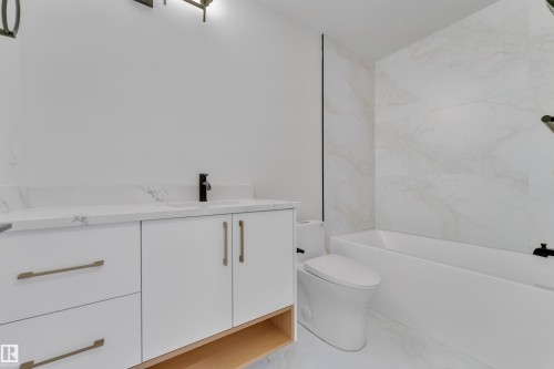 Contemporary bathroom featuring a white vanity with integrated sink, a dark bronze faucet, and a large format tiled tub surround - 6092 179 Ave Nw, Edmonton, AB - Indoor Photo Showing Bathroom