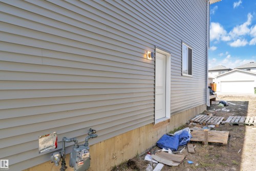 Gray horizontal siding exterior with a white entry door, an exterior wall light fixture, and a single window with white trim - 6092 179 Ave Nw, Edmonton, AB - Outdoor With Exterior