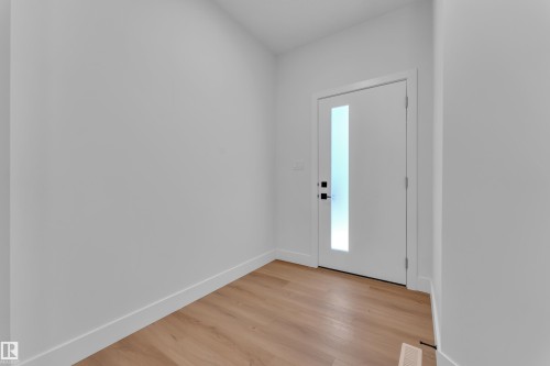 Entryway featuring a contemporary white door with a frosted vertical glass panel, matte black hardware, light wood-finish flooring, white baseboards, and neutral wall tones - 6092 179 Ave Nw, Edmonton, AB - Indoor Photo Showing Other Room