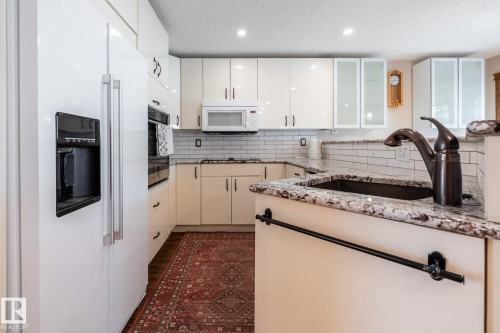 Kitchen featuring a white side-by-side refrigerator, cream-colored cabinetry, light granite countertops, a subway tile backsplash, and recessed lighting - 4632 151 Street, Edmonton, AB - Indoor Photo Showing Kitchen With Upgraded Kitchen
