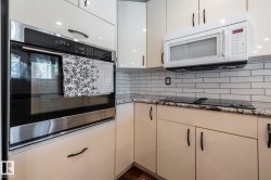Kitchen featuring a built-in stainless steel oven, white cabinetry with black hardware, white subway tile backsplash, granite countertops, and a black cooktop - 