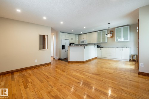 Open-concept kitchen and living area featuring wood-finish flooring, recessed lighting, white cabinetry with glass-front uppers, and stainless steel appliances - 4632 151 Street, Edmonton, AB - Indoor Photo Showing Kitchen