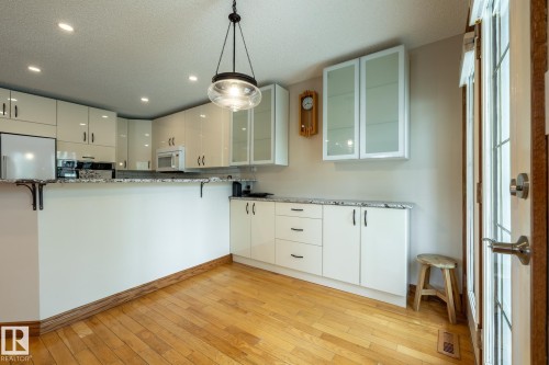 Gourmet kitchen featuring wood-finish flooring, white cabinetry with contemporary pulls, recessed ceiling lighting, granite-look countertops, and a glass-paneled exterior door - 4632 151 Street, Edmonton, AB - Indoor Photo Showing Kitchen