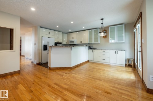 Open-concept kitchen featuring wood-finish flooring, white cabinetry, granite-finish countertops, recessed lighting, and a contemporary pendant light fixture - 4632 151 Street, Edmonton, AB - Indoor Photo Showing Kitchen