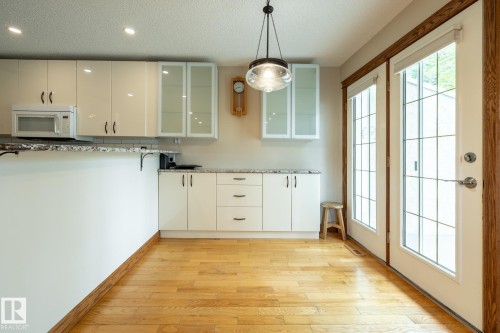 Bright kitchen area featuring light wood-finish flooring, white cabinetry with dark hardware, and granite-style countertops - 4632 151 Street, Edmonton, AB - Indoor