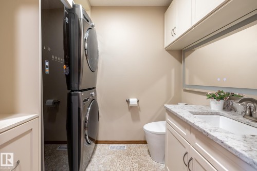 Laundry area with a stacked washer and dryer, complemented by a pebble-finish floor - 4632 151 Street, Edmonton, AB - Indoor Photo Showing Laundry Room