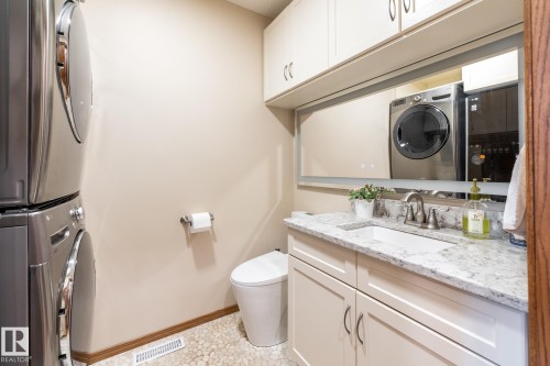 Laundry area featuring stacked appliances, a pebble-finish floor, a compact toilet, a vanity with a light-colored countertop, and integrated upper cabinetry - 4632 151 Street, Edmonton, AB - Indoor Photo Showing Laundry Room
