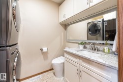 Laundry area featuring stacked appliances, a pebble-finish floor, a compact toilet, a vanity with a light-colored countertop, and integrated upper cabinetry - 