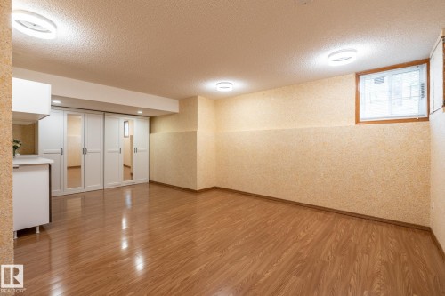 Expansive room featuring wood-finish flooring, recessed lighting, a built-in cabinetry unit with a countertop, and sliding closet doors with mirrored panels - 4632 151 Street, Edmonton, AB - Indoor Photo Showing Other Room