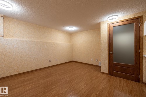 Spacious room featuring wood-finish flooring, textured wall coverings, and contemporary flush-mount lighting - 4632 151 Street, Edmonton, AB - Indoor Photo Showing Other Room