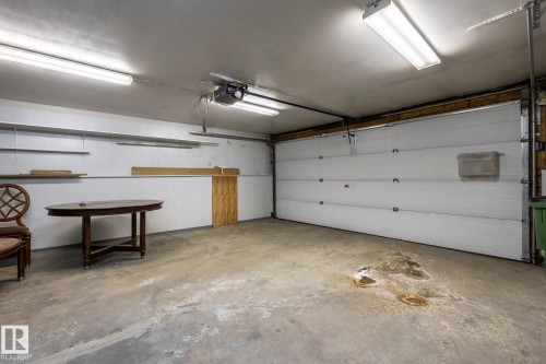 Spacious garage featuring a concrete floor, overhead fluorescent lighting, and a white paneled garage door - 4632 151 Street, Edmonton, AB - Indoor Photo Showing Garage