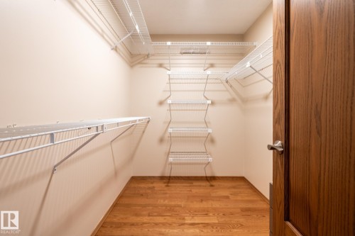 Walk-in closet featuring wire shelving, multiple storage levels, wood-finish flooring, and a paneled wood door with brushed nickel hardware - 4632 151 Street, Edmonton, AB - Indoor With Storage