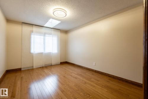 Room featuring hardwood flooring, a window with panel track blinds, a flush mount ceiling light fixture, a ceiling skylight, and neutral wall paint - 4632 151 Street, Edmonton, AB - Indoor Photo Showing Other Room