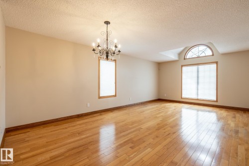 Spacious interior featuring wood-finish flooring throughout, a decorative chandelier, and multiple windows with wood trim and blinds - 4632 151 Street, Edmonton, AB - Indoor Photo Showing Other Room