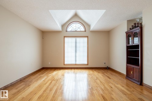 Room featuring wood-finish flooring, a large window with blinds, and an arched transom window above - 4632 151 Street, Edmonton, AB - Indoor Photo Showing Other Room